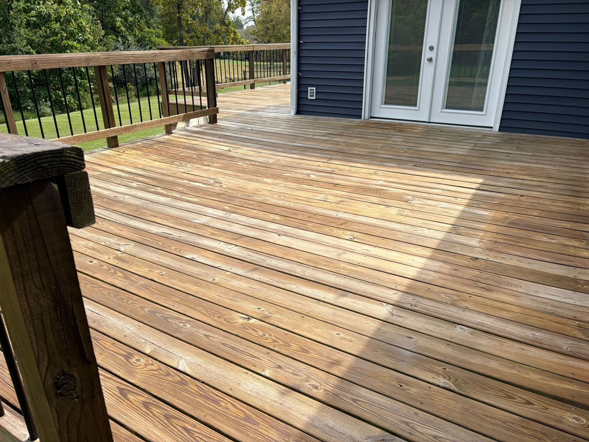 Cleaned wooden deck with black balusters beside a navy house