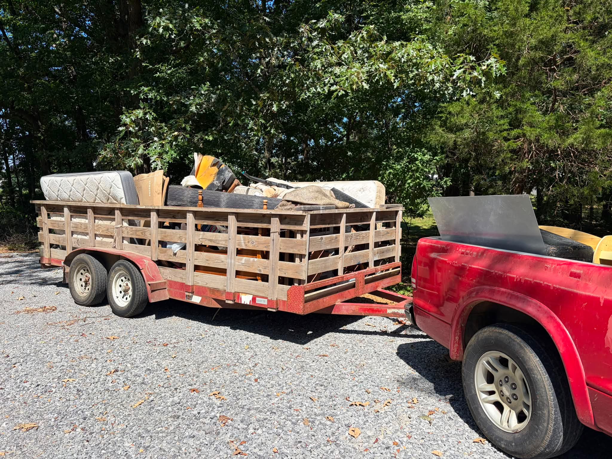 Trailer loaded with old mattresses and furniture behind a red pickup