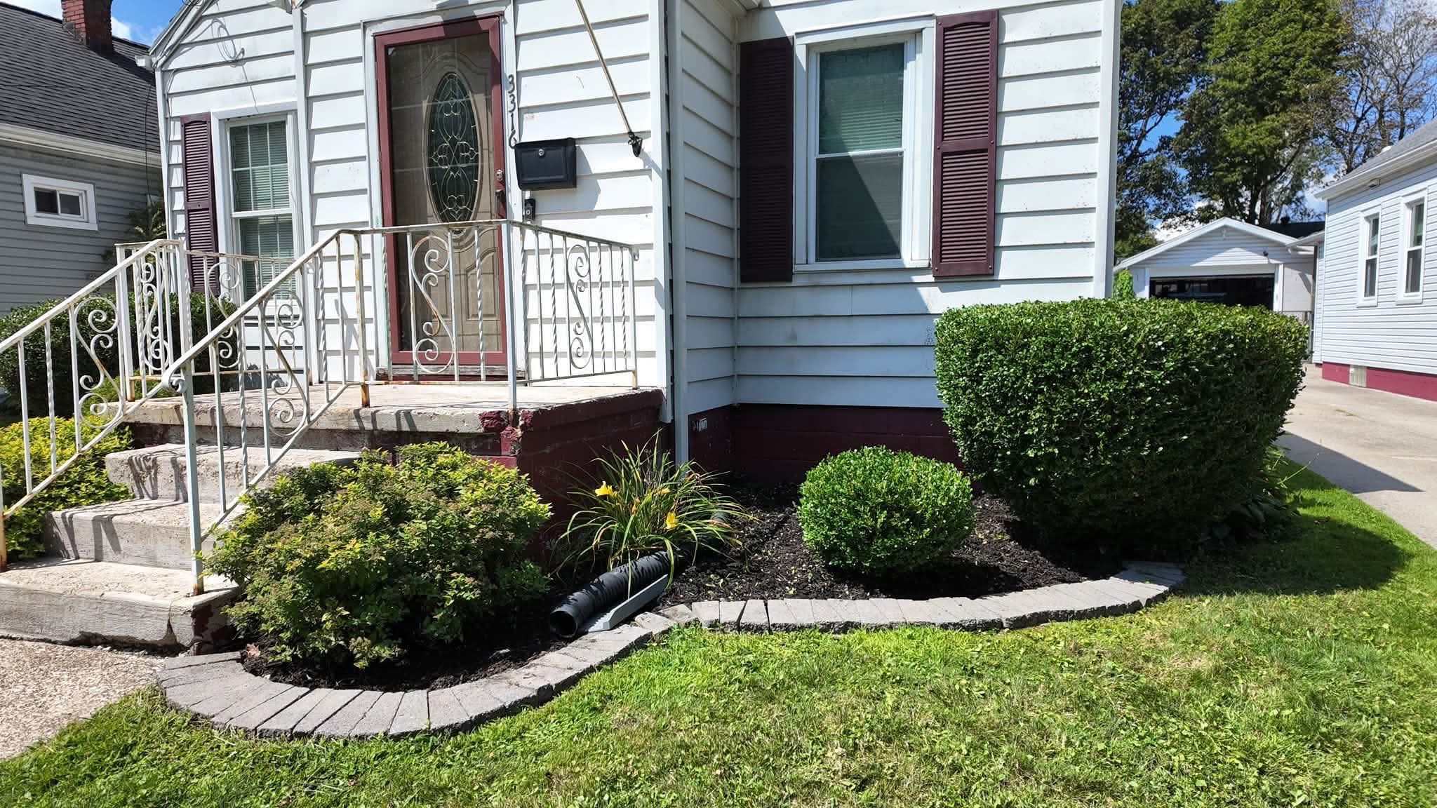 Fresh mulch bed with paver edging and trimmed shrubs by a white house